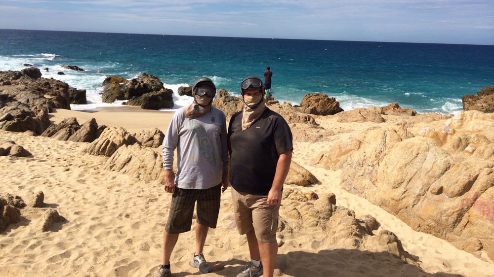 Two ATV riders standing at the beach